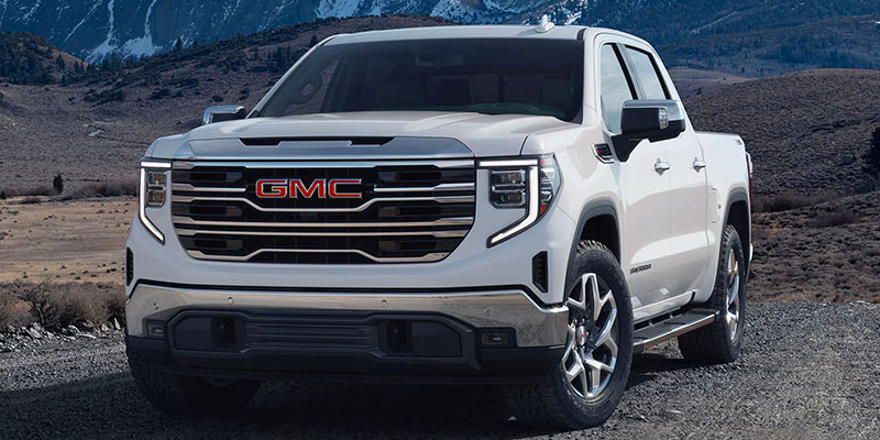 2025 GMC Sierra 1500 pickup truck in white parked on a rugged mountain road, highlighting its bold front grille, LED headlights, and premium exterior design.